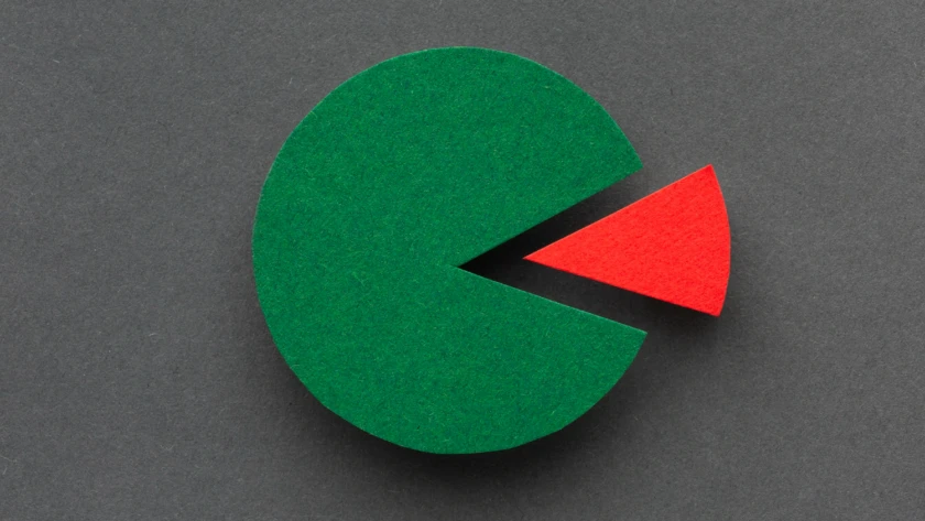 Paper pie chart featuring a large green circle and a small detached red slice on a dark-grey background, symbolising market-share opportunity.