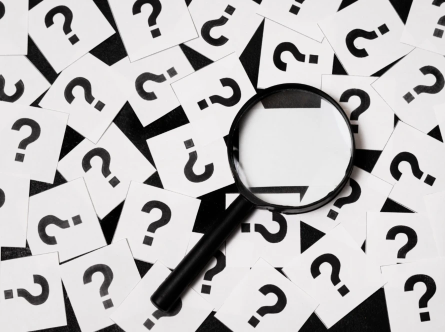 Magnifying glass lying on scattered white cards printed with bold black question marks.