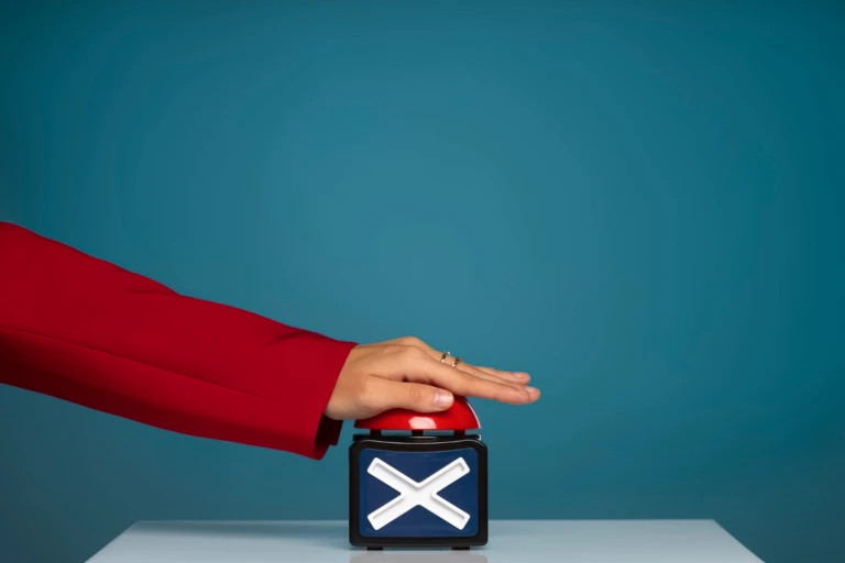 Hand in a red blazer pressing a large red buzzer on a box with a white “X,” against a teal background.